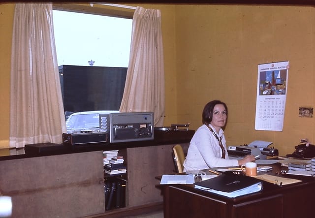 A staffer at her desk with a tape machine on the window ledge